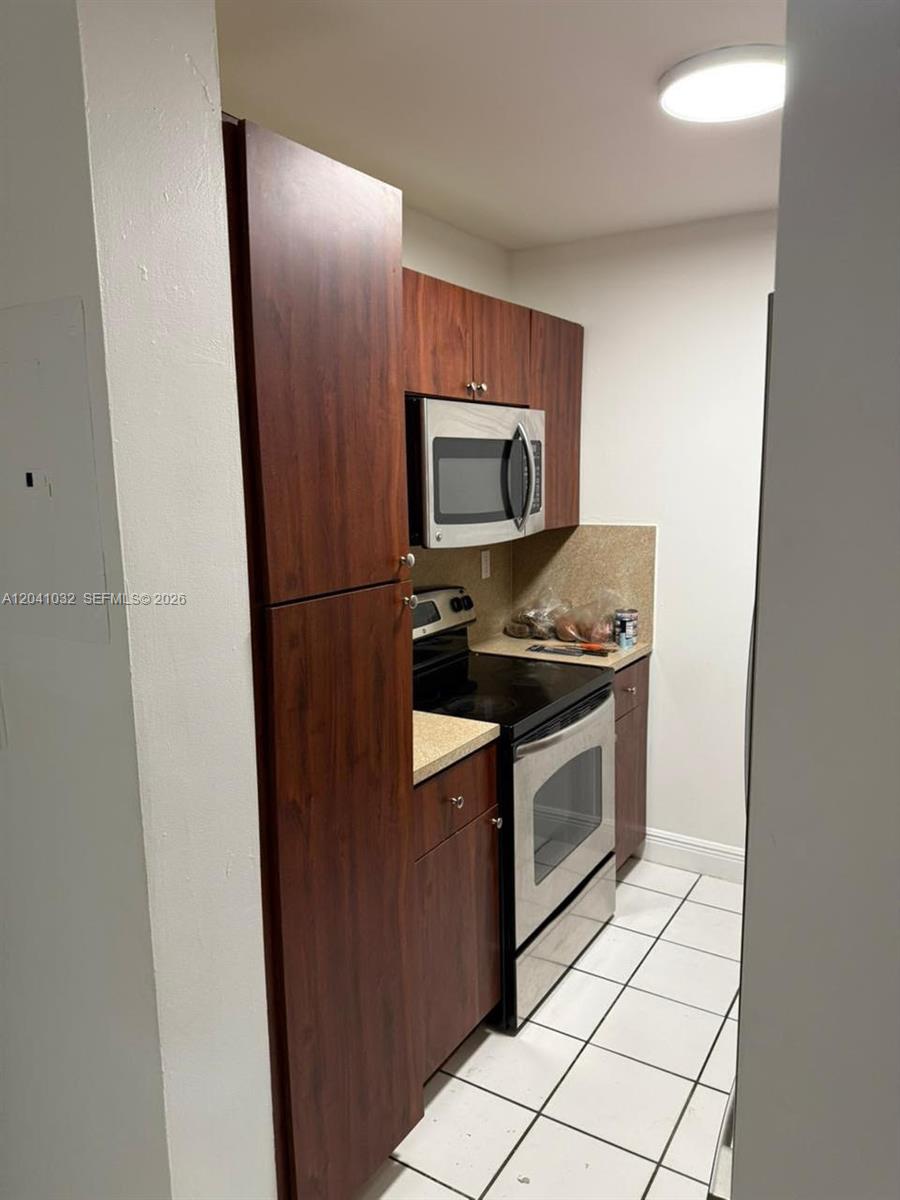A galley kitchen features dark wood cabinets, stainless steel appliances, and white tiled flooring — 600 NW 32nd Pl # 303, Miami FL 33125, MIAMI, FL
