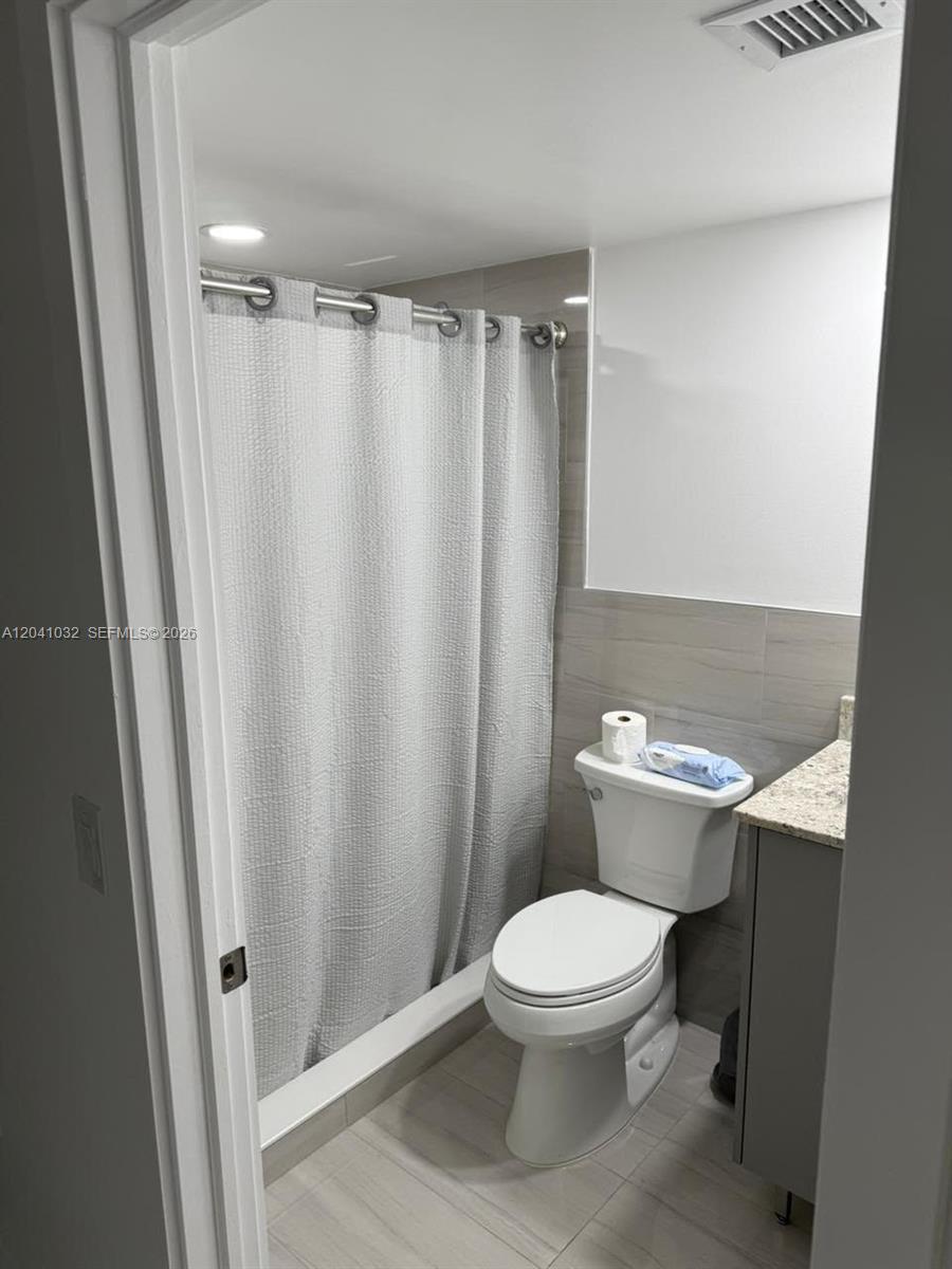 A bathroom features a walk-in shower with a gray curtain, a toilet, and a vanity — 600 NW 32nd Pl # 303, Miami FL 33125, MIAMI, FL