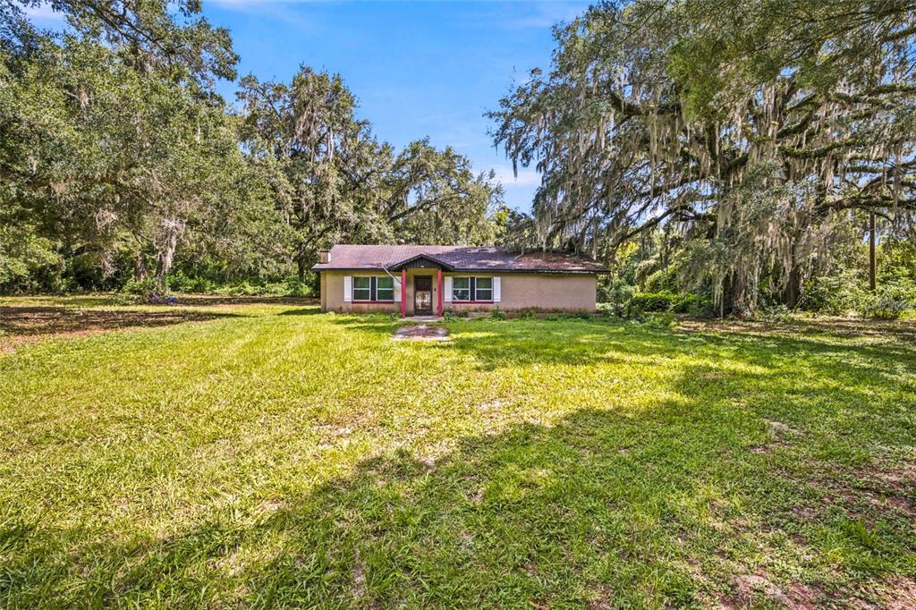 A single-story house with a brown roof sits on a large lawn under oak trees — 5398 SE 141ST STREET, SUMMERFIELD, FL
