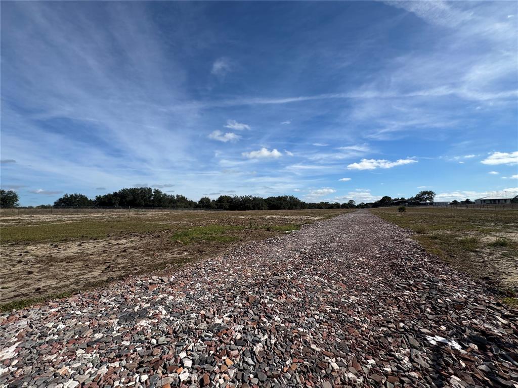 A gravel driveway leads through a large, flat, open field under a blue sky — 4547 GLENN SAINT MARY ROAD, LAKE WALES, FL
