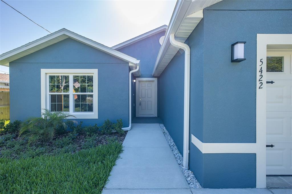 A blue house exterior features a white-trimmed window, a front door, and a garage — 5422 CHARLES STREET, NEW PORT RICHEY, FL