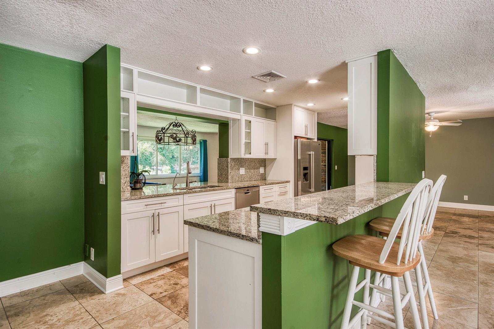 A kitchen features white cabinets, granite countertops, green walls, and a breakfast bar with stools — 11065 164th Court N, Jupiter FL 33478, JUPITER, FL