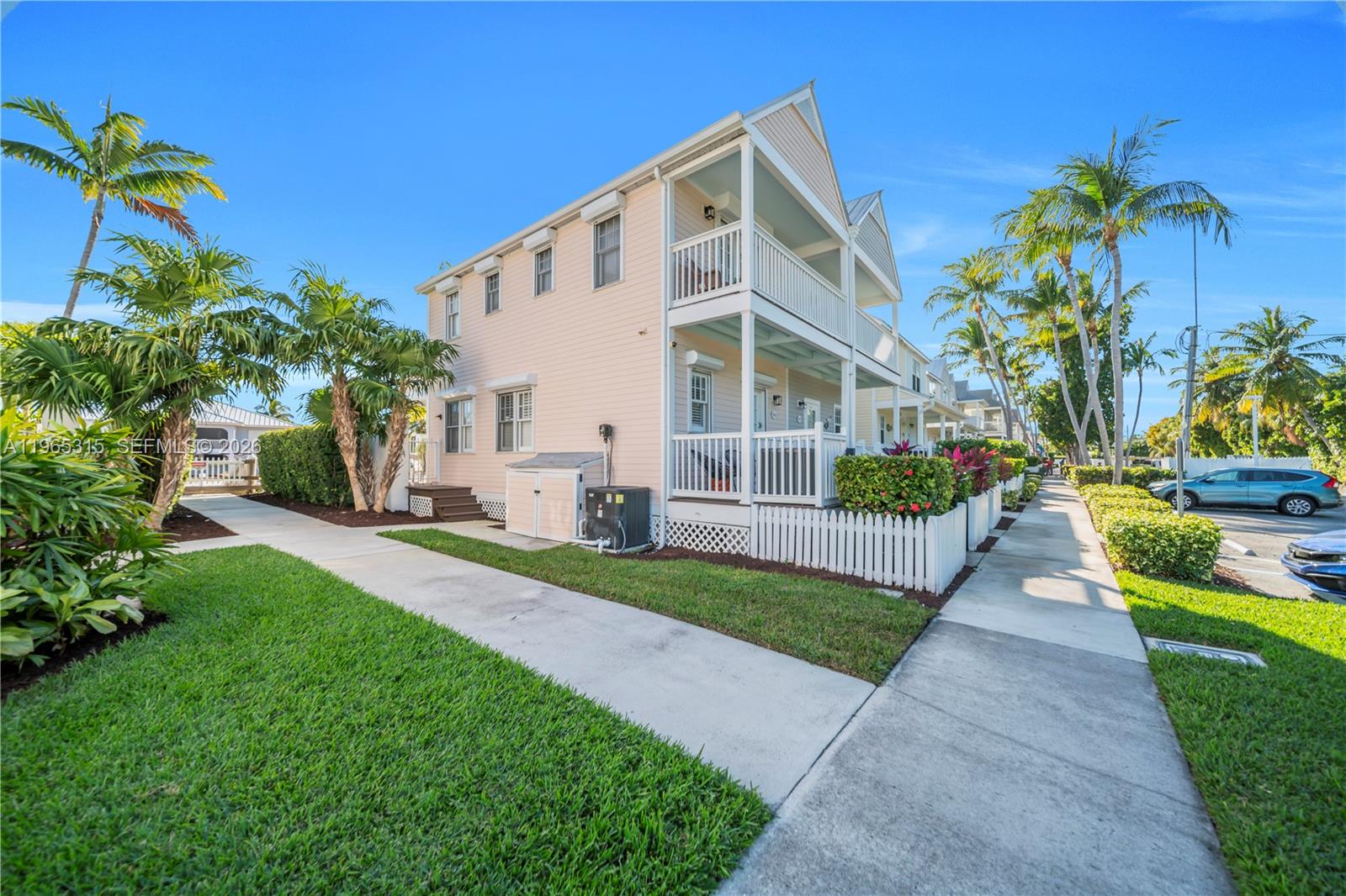 A light-colored two-story townhouse features a white picket fence, balconies, and surrounding palm trees — 7026 Harbor Village Dr, Duck FL 33050, DUCK, FL