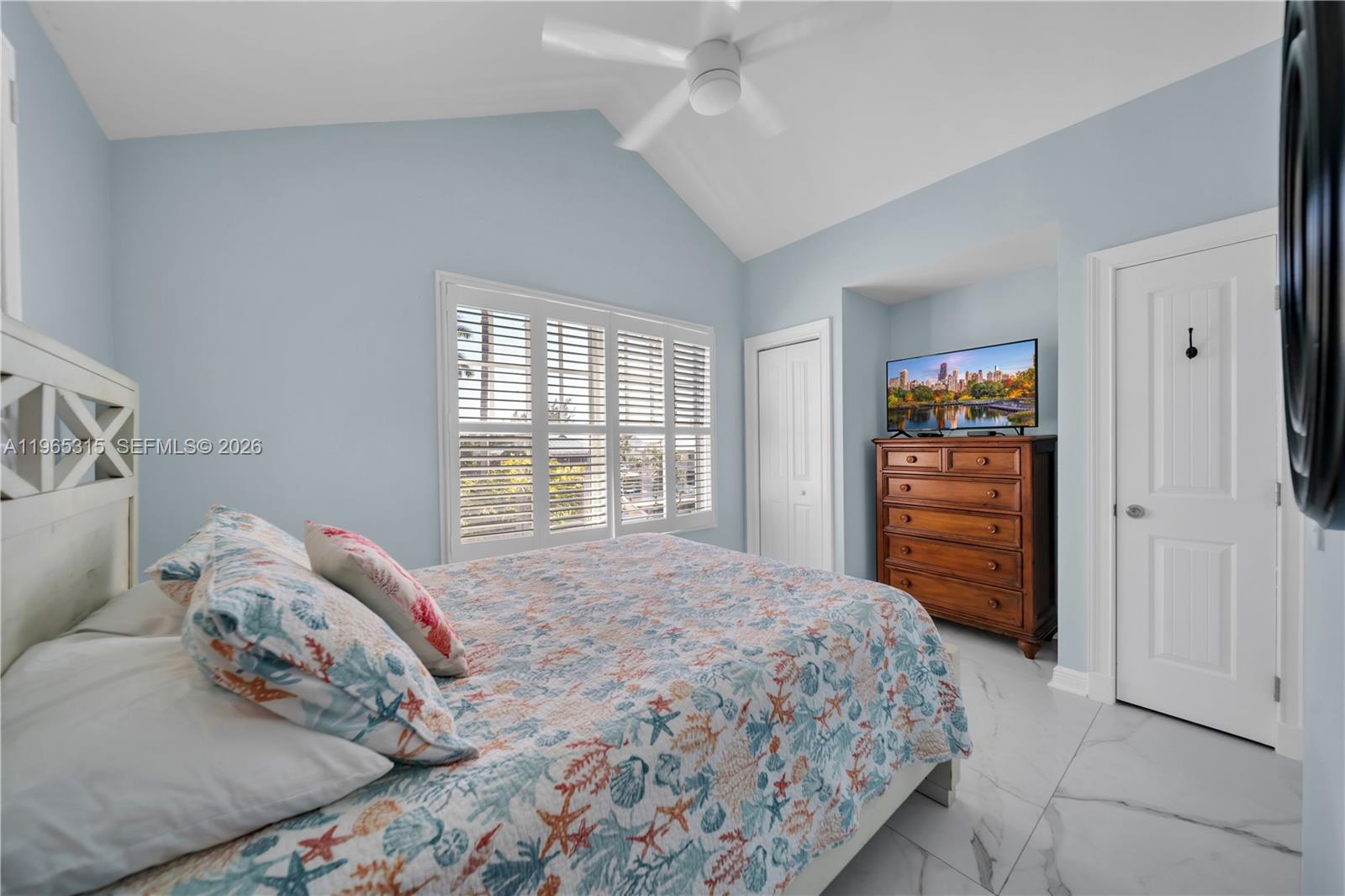 A bedroom features a vaulted ceiling, light blue walls, a patterned quilt, and tile flooring — 7026 Harbor Village Dr, Duck FL 33050, DUCK, FL