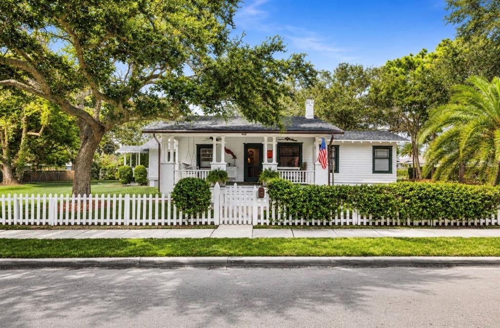 A white cottage-style house with a front porch and picket fence sits behind a lawn — 458 SCOTLAND STREET, DUNEDIN, FL