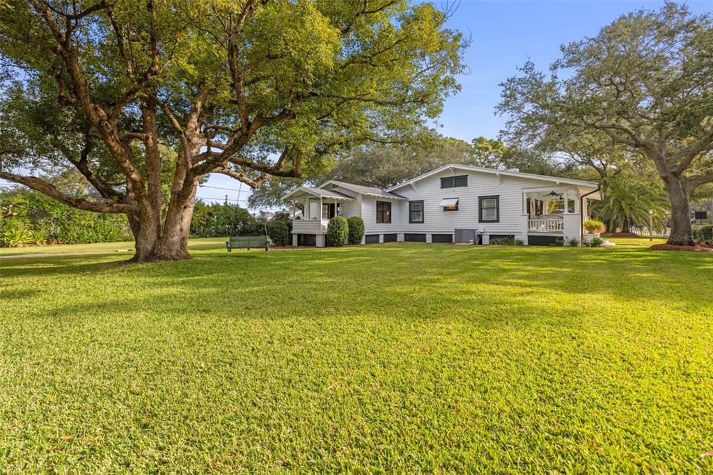 A white, single-story house with a porch sits on a large, grassy lawn with trees — 458 SCOTLAND STREET, DUNEDIN, FL