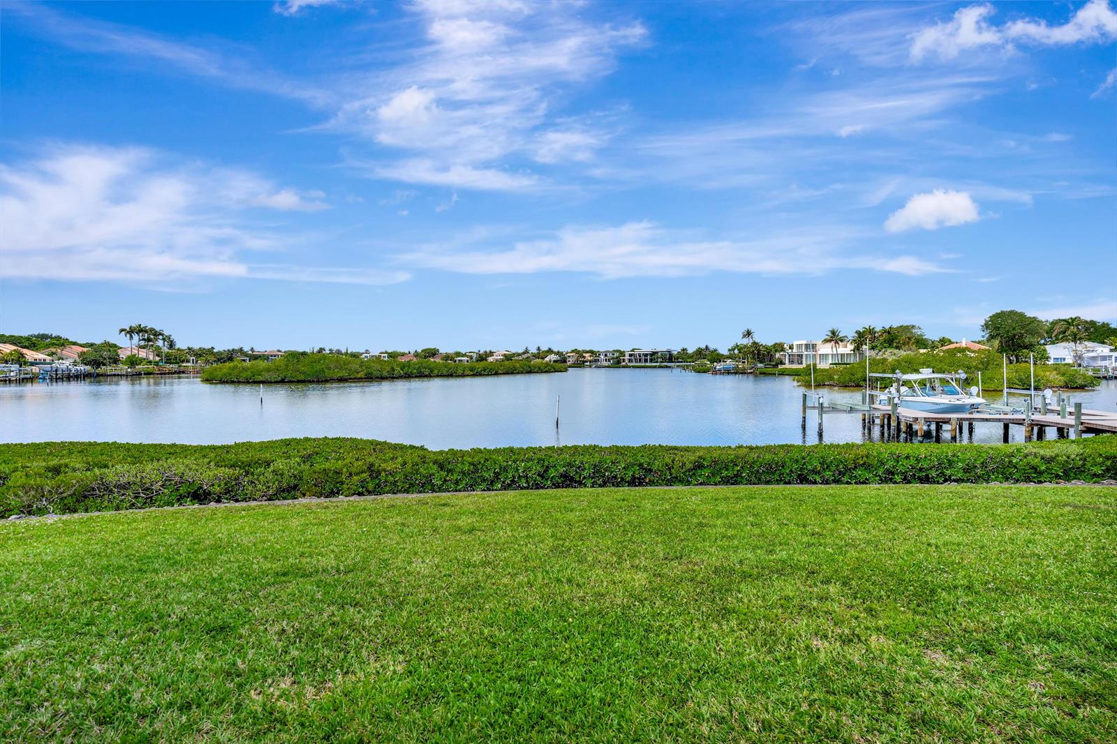 A grassy lawn overlooks a calm bay with a private boat dock and distant houses — 2704 Captains Way, Jupiter FL 33477, JUPITER, FL