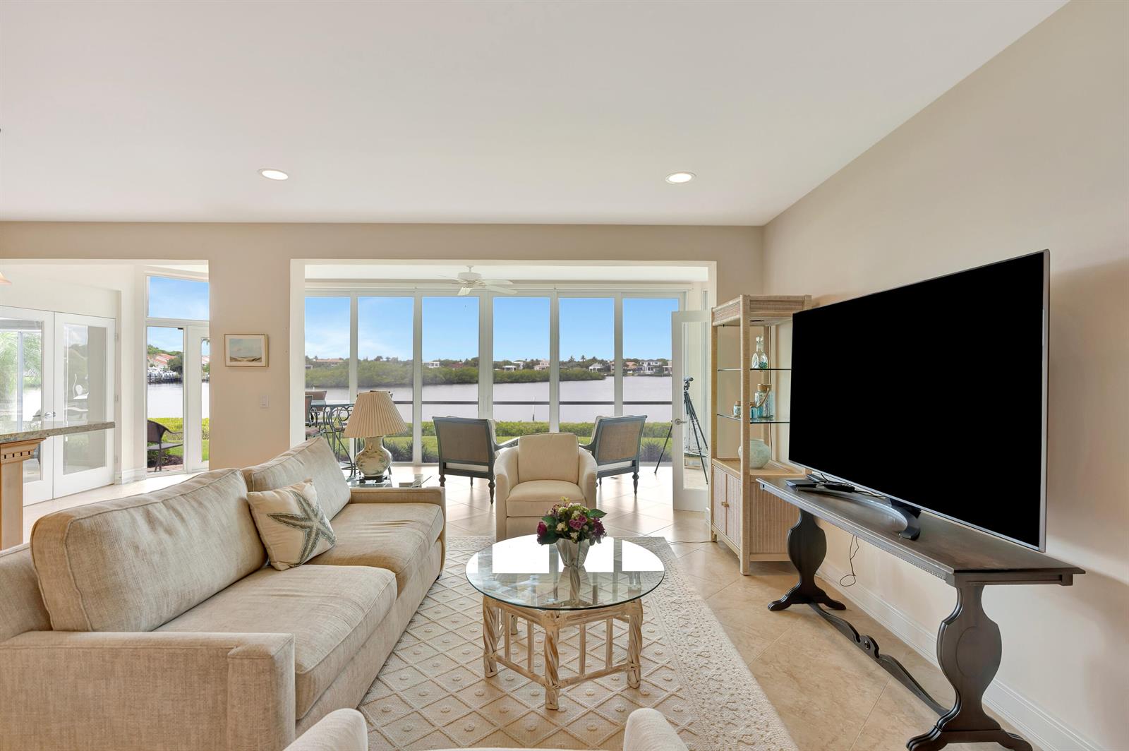 A living room features a large television, beige sofa, and floor-to-ceiling windows overlooking water — 2704 Captains Way, Jupiter FL 33477, JUPITER, FL