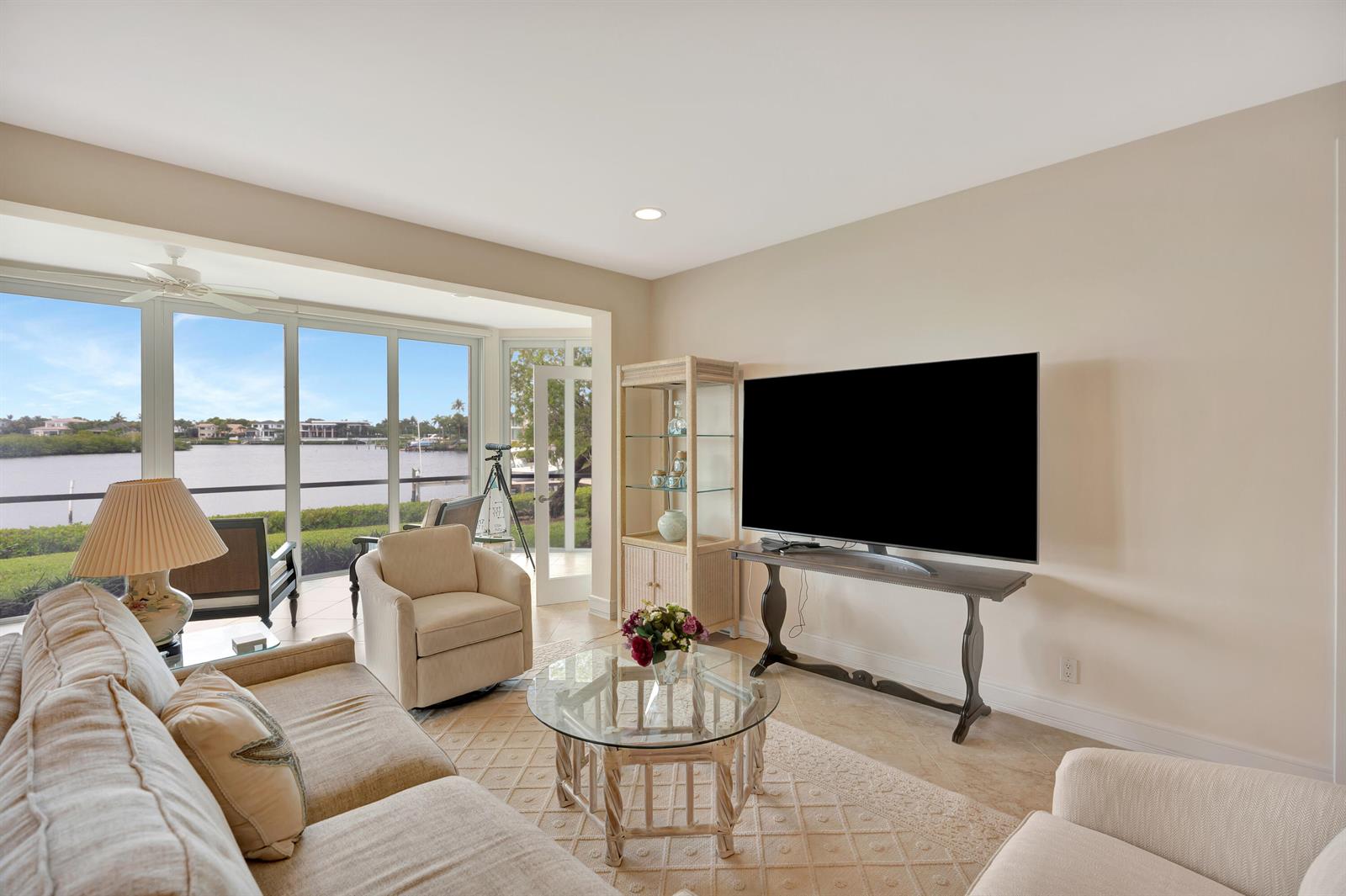 A living room with a large television, beige furniture, and a view of the water — 2704 Captains Way, Jupiter FL 33477, JUPITER, FL
