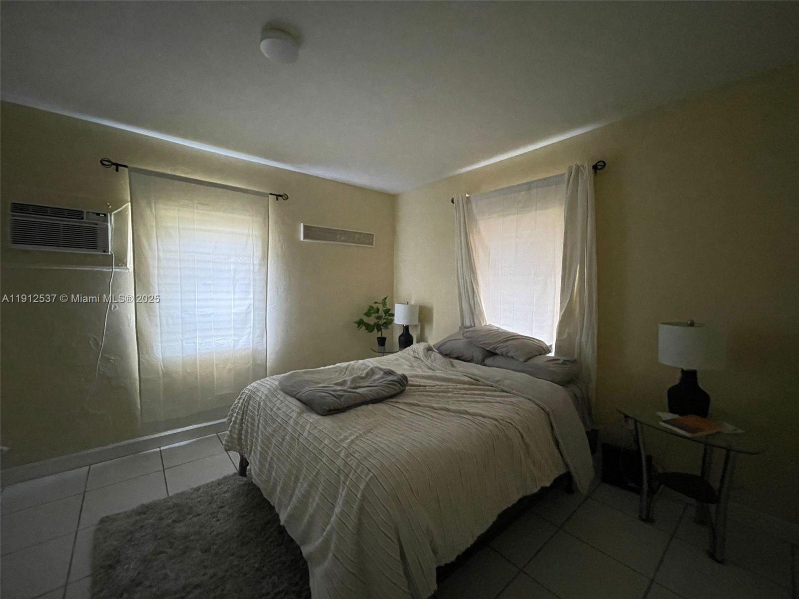 A bedroom features a bed, two windows with white curtains, and tile flooring — 55 NW 69th St, Miami FL 33150, MIAMI, FL