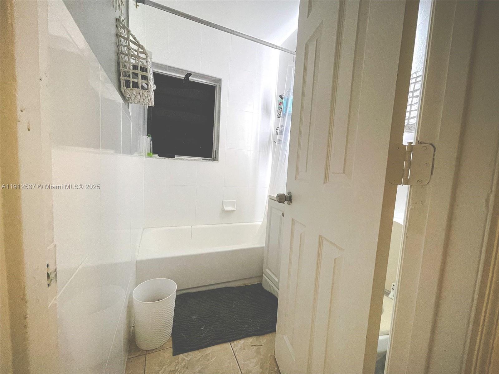 A bathroom features a white bathtub, tiled walls, a window, and a white door — 55 NW 69th St, Miami FL 33150, MIAMI, FL