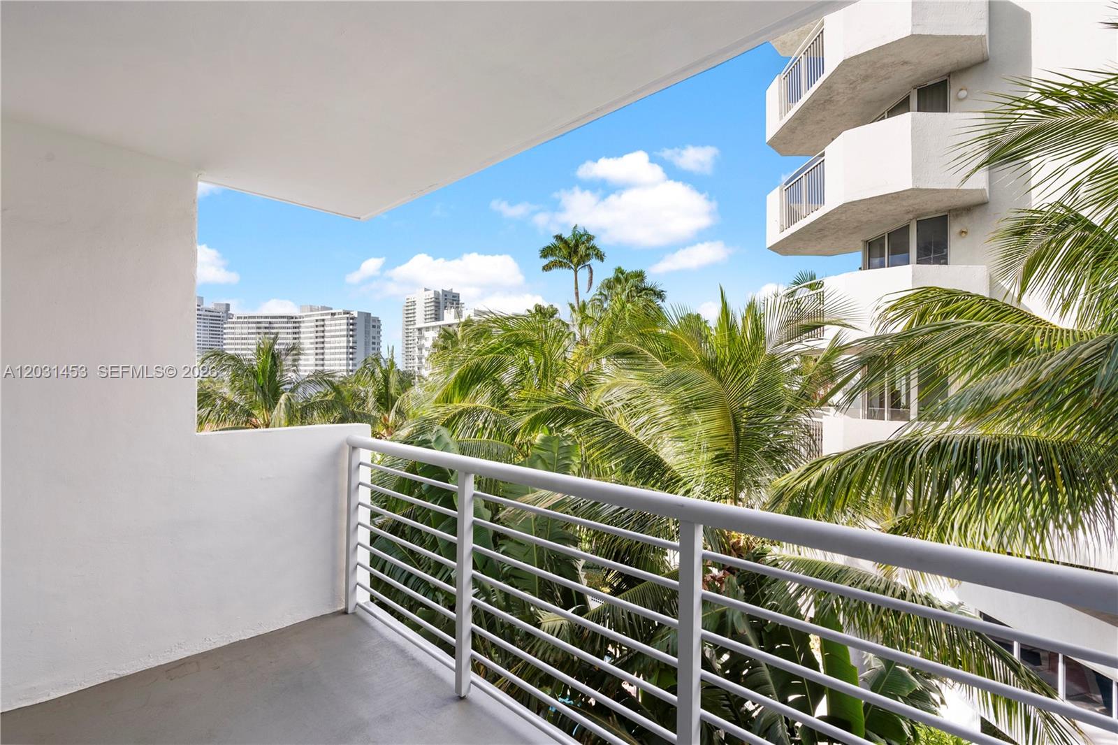 A balcony with white railings overlooks palm trees and neighboring high-rise buildings — 1605 Bay Rd # 503, Miami Beach FL 33139, MIAMI BEACH, FL