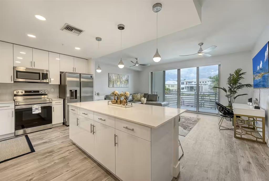 A modern kitchen with white cabinetry, a large island, and an open-concept living area — 1709 N TAMIAMI TRAIL UNIT 220, SARASOTA, FL