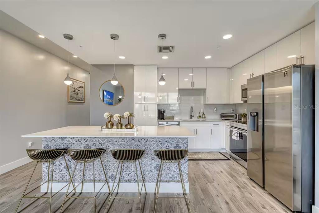 A modern kitchen features white cabinetry, stainless steel appliances, and a patterned island with barstools — 1709 N TAMIAMI TRAIL UNIT 220, SARASOTA, FL