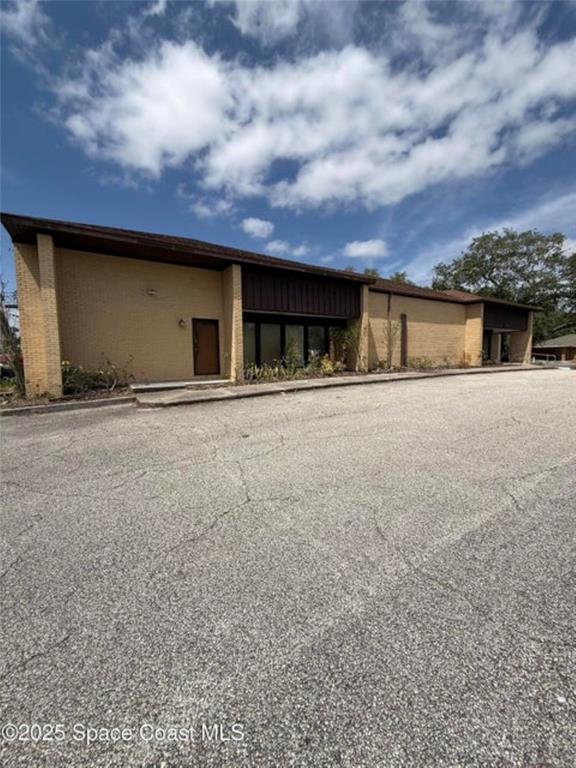 A low-rise commercial building with a tan brick facade and a large asphalt parking lot — 1855 JESS PARRISH COURT, TITUSVILLE, FL