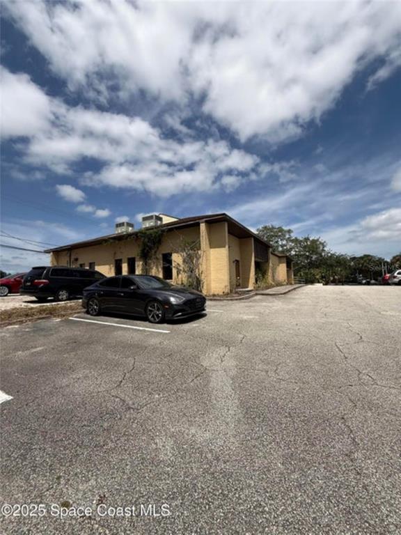 A tan commercial building with a parking lot in the foreground under a cloudy sky — 1855 JESS PARRISH COURT, TITUSVILLE, FL