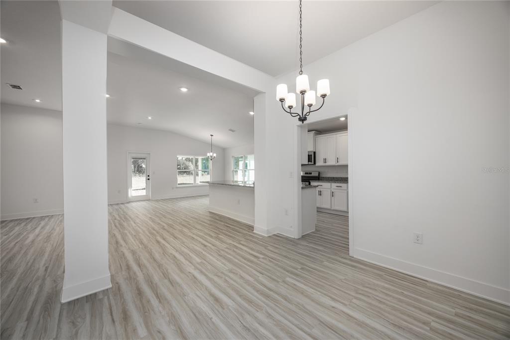 An open-concept dining area with a chandelier leads to a kitchen and living space — 581 SW BELLFLOWER DRIVE, LAKE CITY, FL