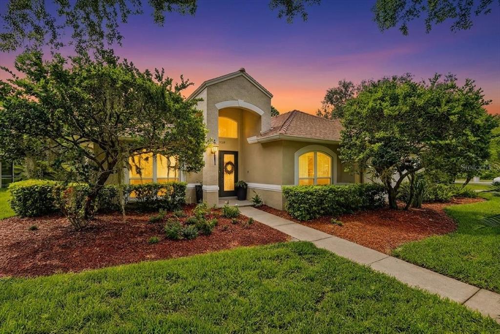 A single-story stucco house with a covered entryway and arched windows at sunset — 5539 AVENUE DU SOLEIL, LUTZ, FL