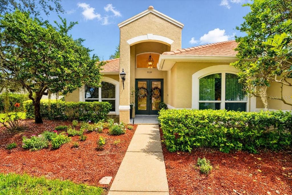 A single-story house with a tan stucco exterior, arched entryway, and a paved walkway — 5539 AVENUE DU SOLEIL, LUTZ, FL
