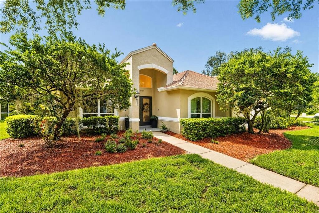 A single-story tan stucco house with a tiled roof and a paved walkway to the entrance — 5539 AVENUE DU SOLEIL, LUTZ, FL