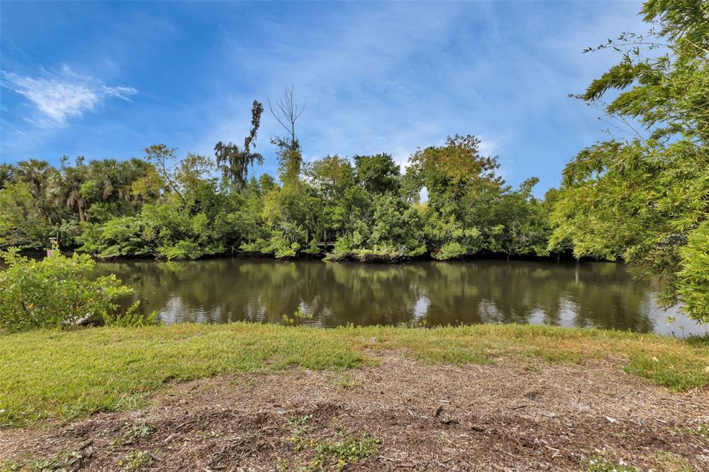 A grassy bank overlooks a calm, dark river lined with dense trees and vegetation — 3410, 3402, 3420 COLONY COURT, PUNTA GORDA, FL
