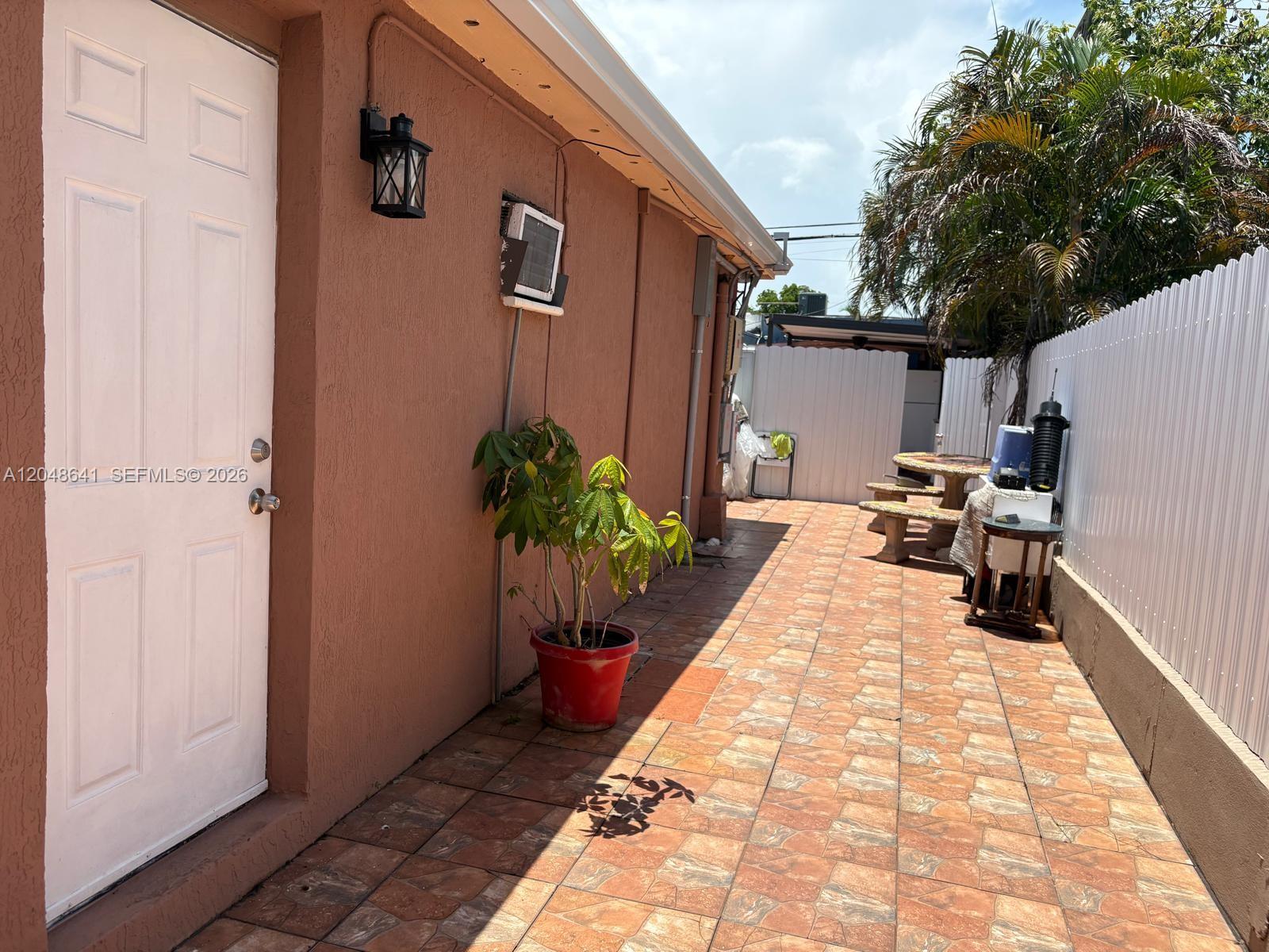 A paved outdoor patio area features a white door, a potted plant, and outdoor seating — 6444 Fletcher St, Hollywood FL 33023, HOLLYWOOD, FL