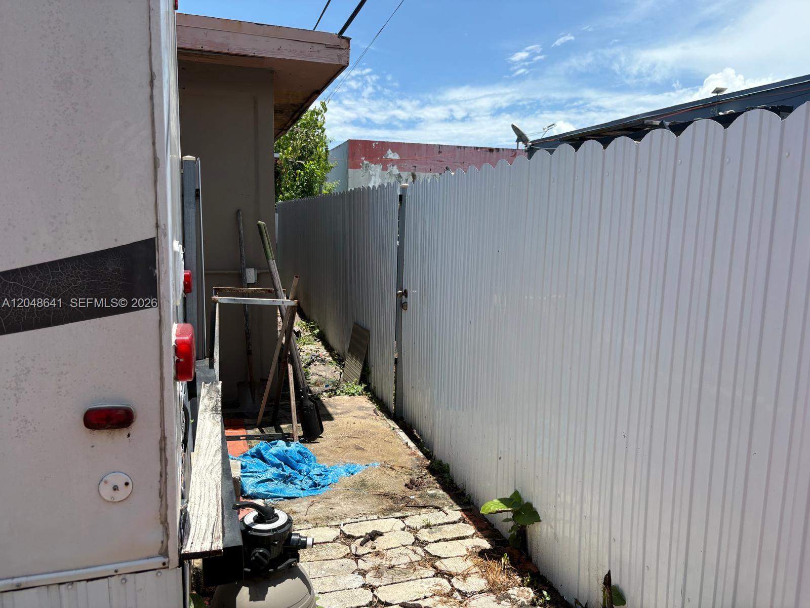 A narrow outdoor side yard features a white fence, a trailer, and scattered tools — 6444 Fletcher St, Hollywood FL 33023, HOLLYWOOD, FL