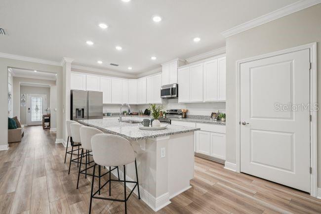 A modern kitchen features white cabinets, granite countertops, a center island with stools, and wood-look flooring — 3040 SUNSCAPE TERRACE, GROVELAND, FL