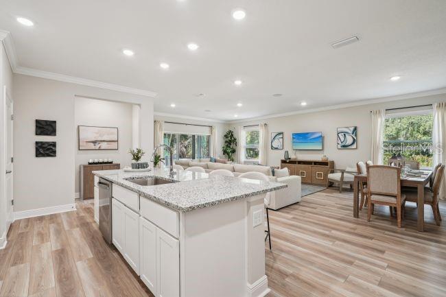 An open-concept kitchen with a granite island overlooks a living room and dining area — 3040 SUNSCAPE TERRACE, GROVELAND, FL