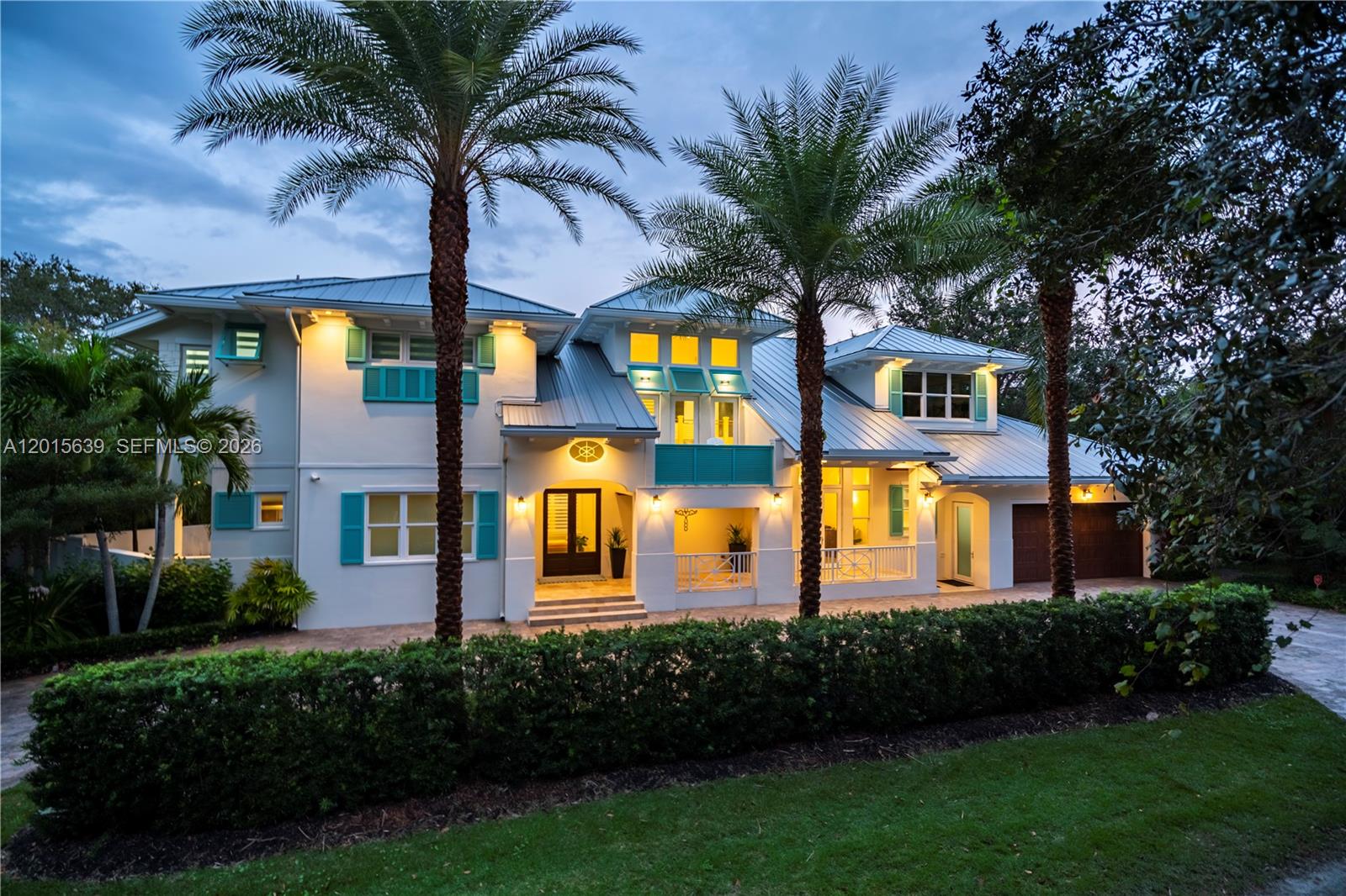 A two-story house with a metal roof, turquoise shutters, and palm trees at dusk — 545 SW Indianola St, Stuart FL 34994, STUART, FL