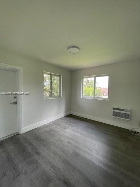 An empty room features gray wood-look flooring, white walls, two windows, and a wall-mounted air conditioner — 1920 NW 151st St # 3, Opa-Locka FL 33054, OPA-LOCKA, FL