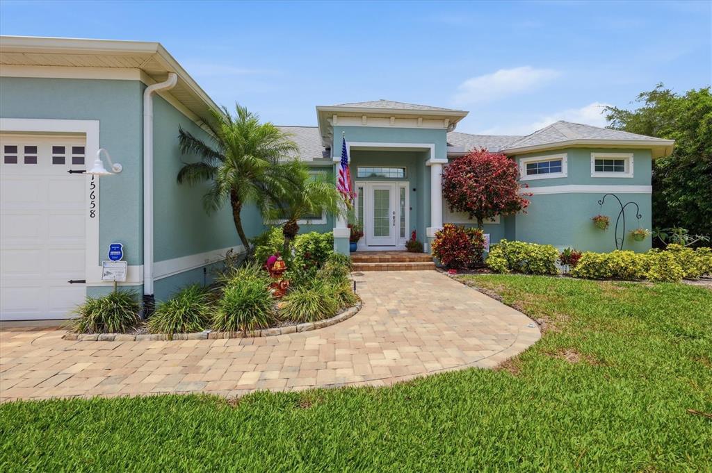 A light blue house with a paver walkway, a palm tree, and a front-facing garage — 15658 APPLEWHITE CIRCLE, PORT CHARLOTTE, FL