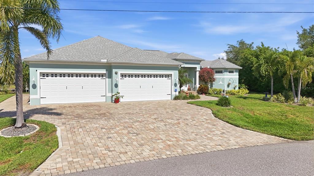 A light green house with a paver driveway and a three-car garage under a clear sky — 15658 APPLEWHITE CIRCLE, PORT CHARLOTTE, FL
