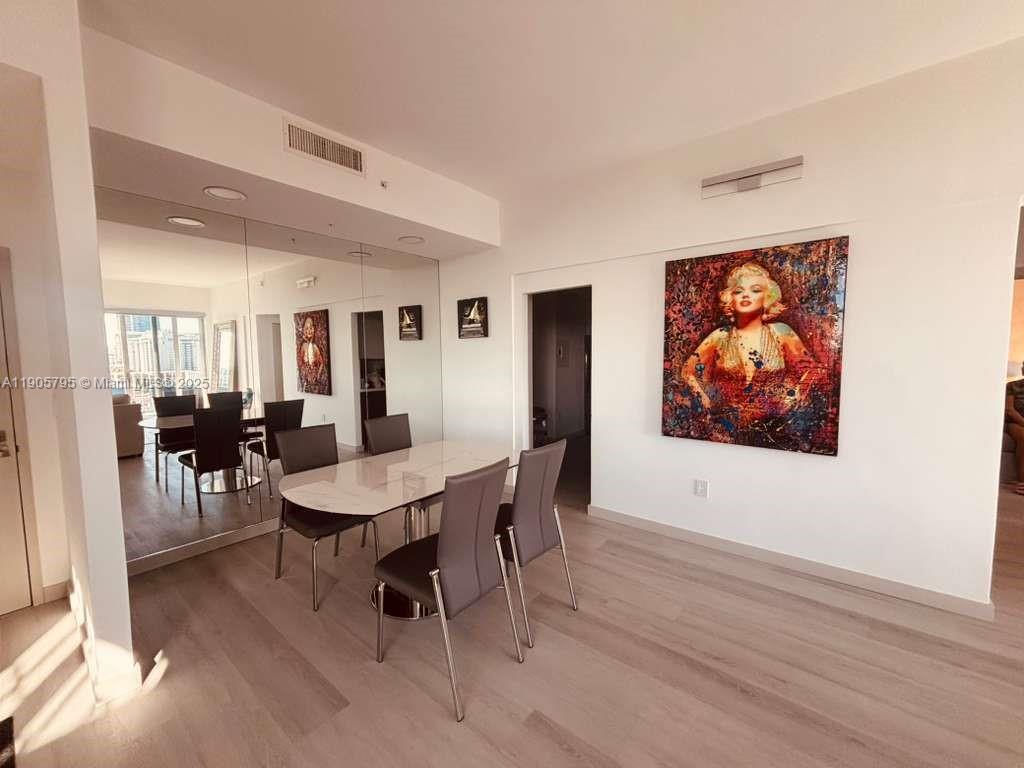A dining room features a white table, modern chairs, a large mirror, and wall art — 2829 Indian Creek Dr # 1403, Miami Beach FL 33140, MIAMI BEACH, FL