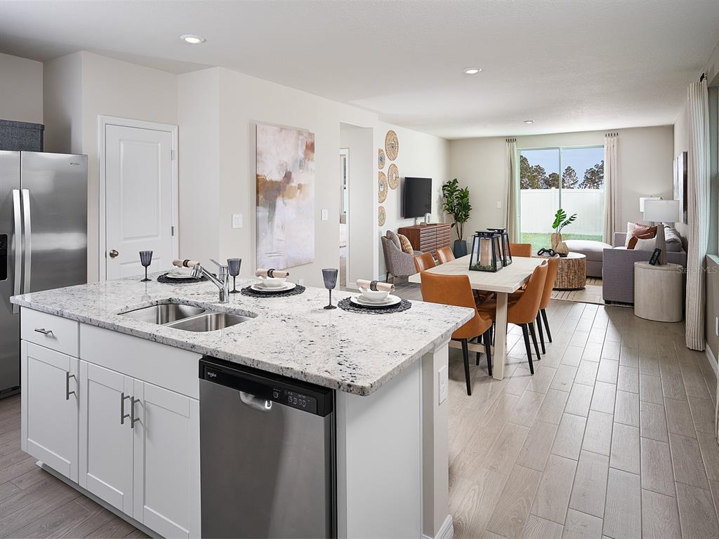 A kitchen island with a stainless steel dishwasher overlooks an open-concept dining and living area — 1524 BREKEY WAY, ZEPHYRHILLS, FL