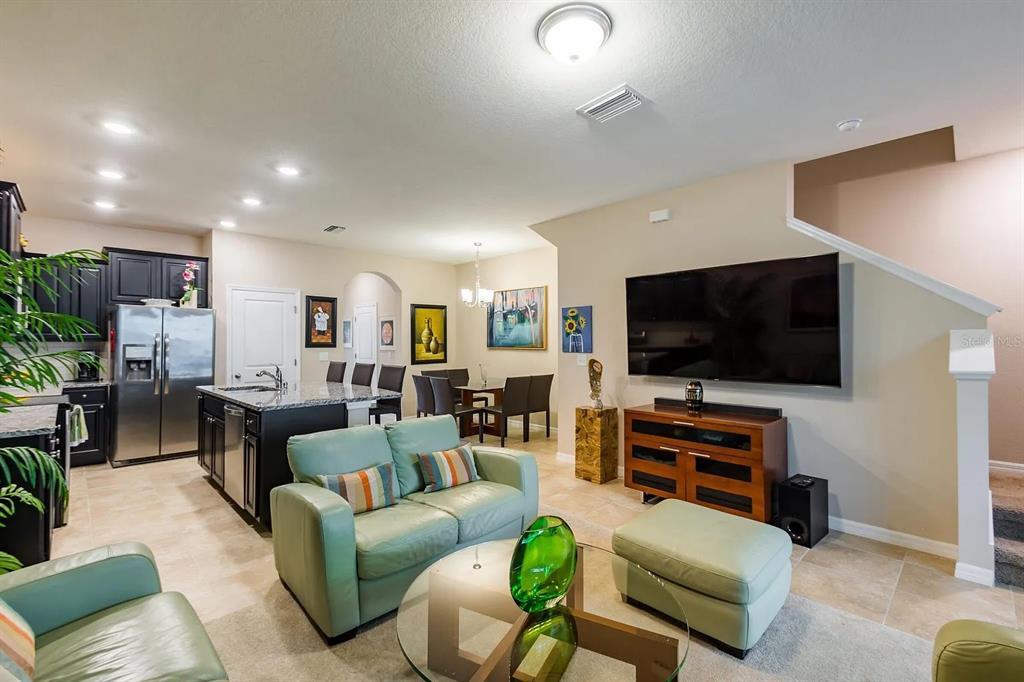 An open-concept living room and kitchen featuring light tile floors and a large television — 8688 ICE WINE STREET, SARASOTA, FL