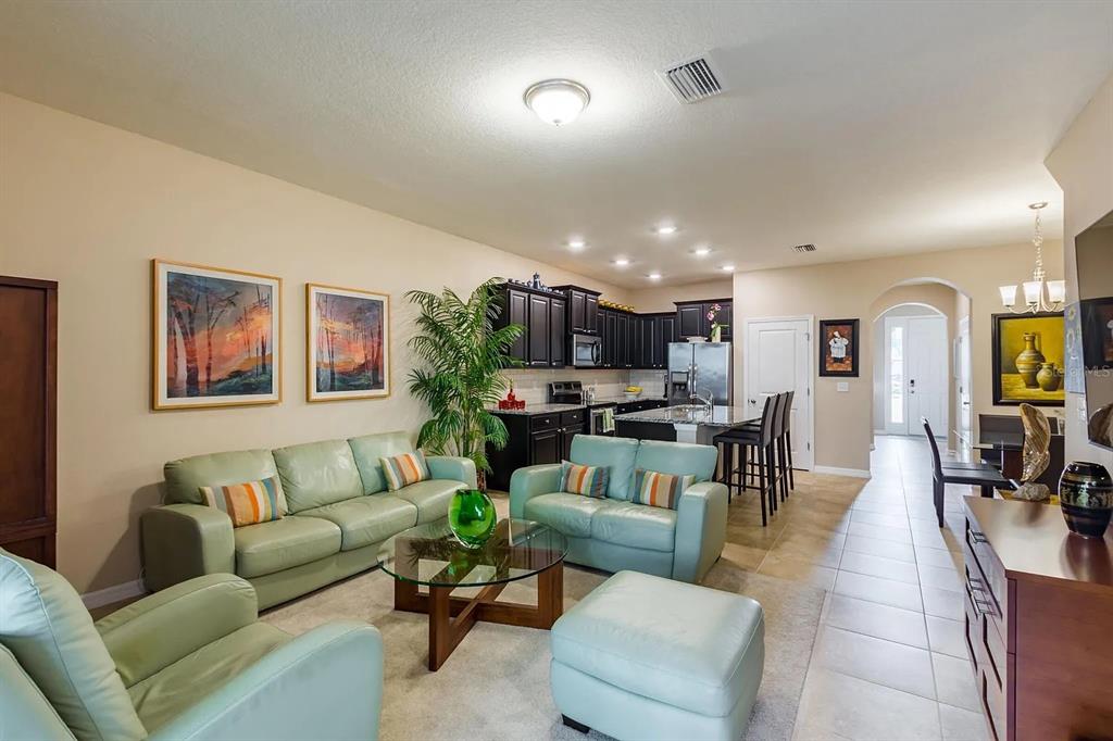 A living room with light green leather furniture, a glass coffee table, and an open kitchen — 8688 ICE WINE STREET, SARASOTA, FL
