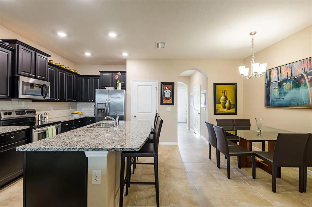 A kitchen with dark cabinets, granite countertops, and an island next to a dining area — 8688 ICE WINE STREET, SARASOTA, FL