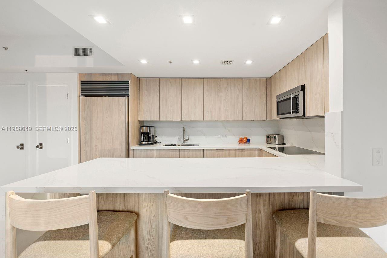 A modern kitchen features light wood cabinetry, a white countertop island, and stainless steel appliances — 6899 Collins Ave # 1810, Miami Beach FL 33141, MIAMI BEACH, FL