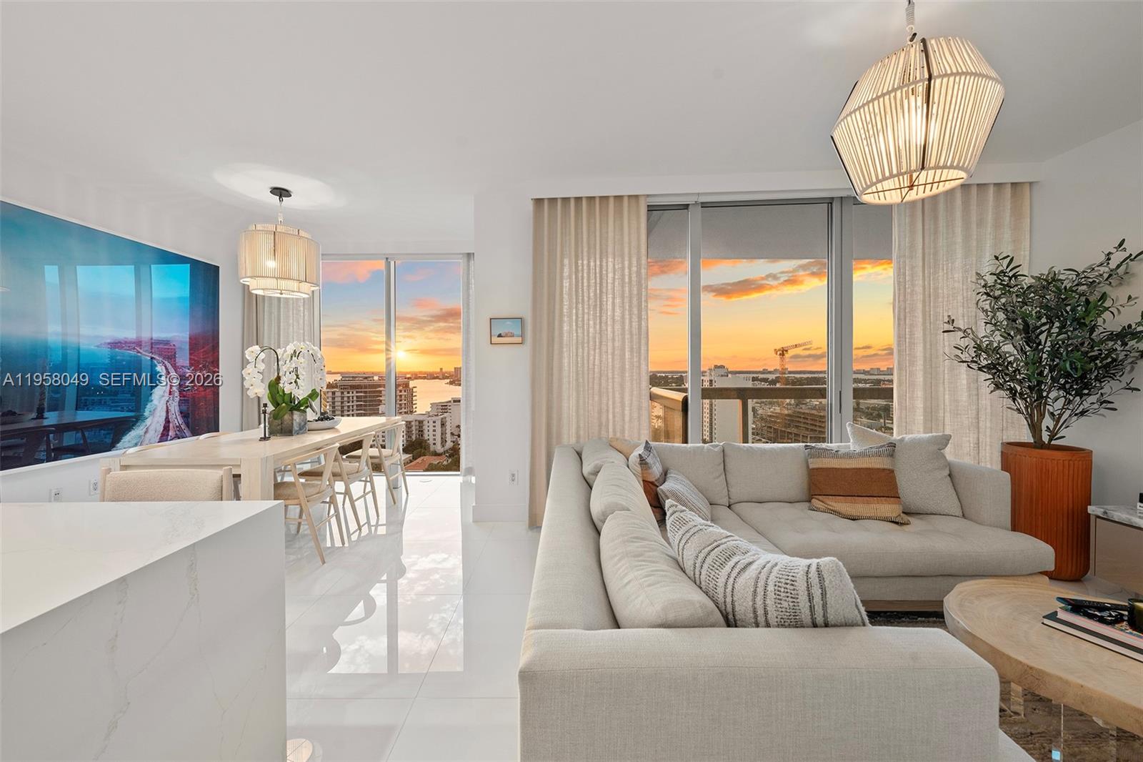 A modern living and dining area features white tile floors, floor-to-ceiling windows, and sunset views — 6899 Collins Ave # 1810, Miami Beach FL 33141, MIAMI BEACH, FL