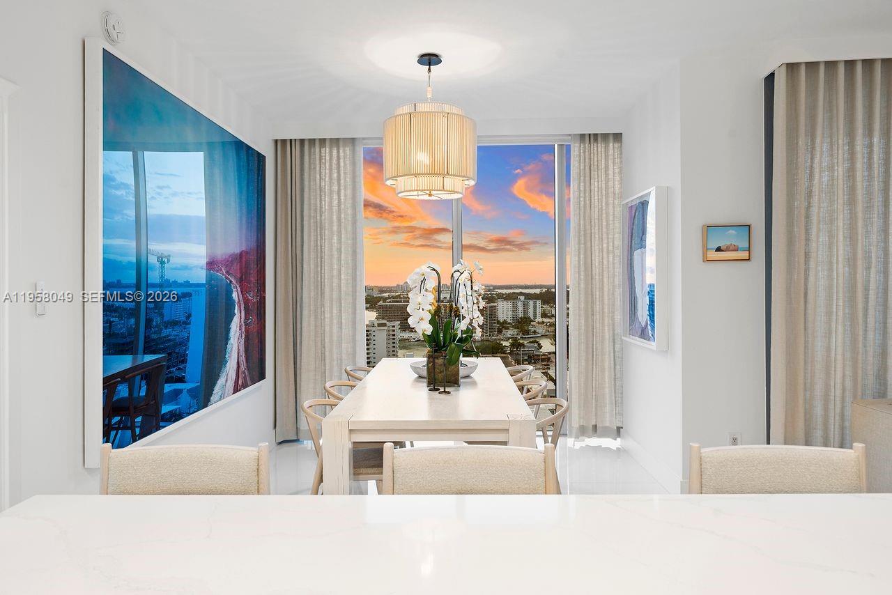 A dining room features a long white table, modern pendant lighting, and floor-to-ceiling windows — 6899 Collins Ave # 1810, Miami Beach FL 33141, MIAMI BEACH, FL