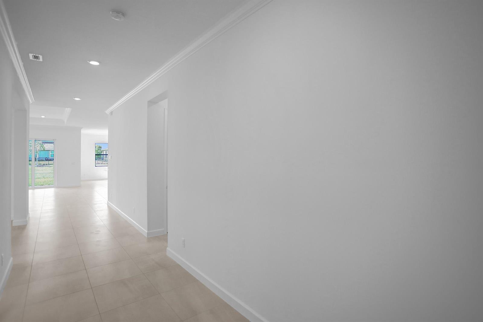 A long, white-walled hallway with light-colored tile flooring leads toward a bright, open living area — 19411 Broad Shore Walk, FL 33470, FL