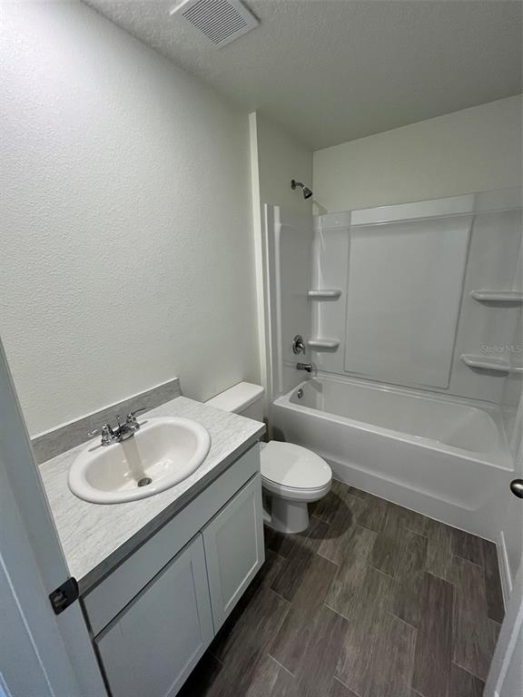 A bathroom features a white vanity, a toilet, and a shower-tub combination with gray flooring — 10115 MCMAHON AVENUE, HASTINGS, FL