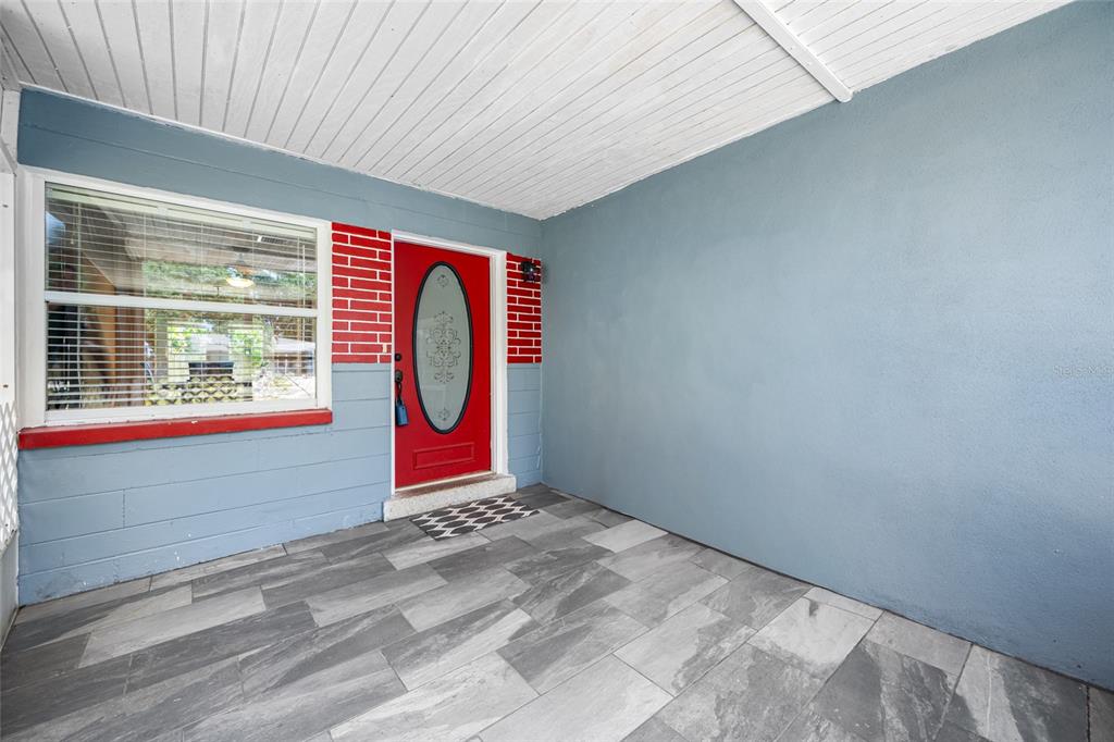 A covered porch features blue walls, a red front door, and gray tiled flooring — 3748 15TH AVENUE SE, LARGO, FL