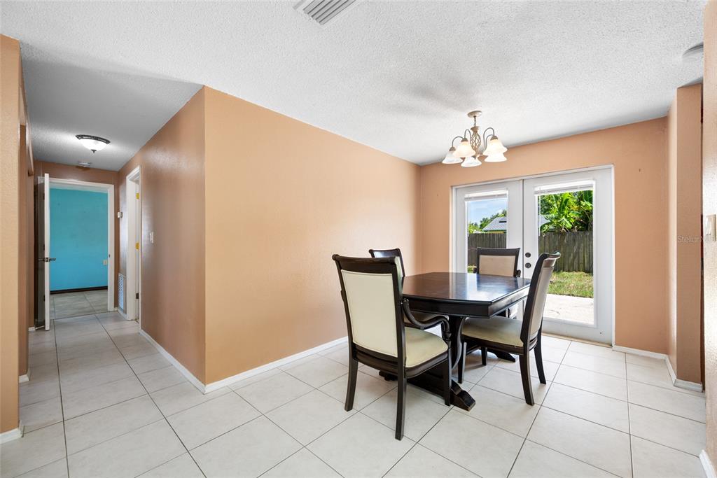 A dining room features tan walls, white tile flooring, a dark table, and glass doors — 3748 15TH AVENUE SE, LARGO, FL