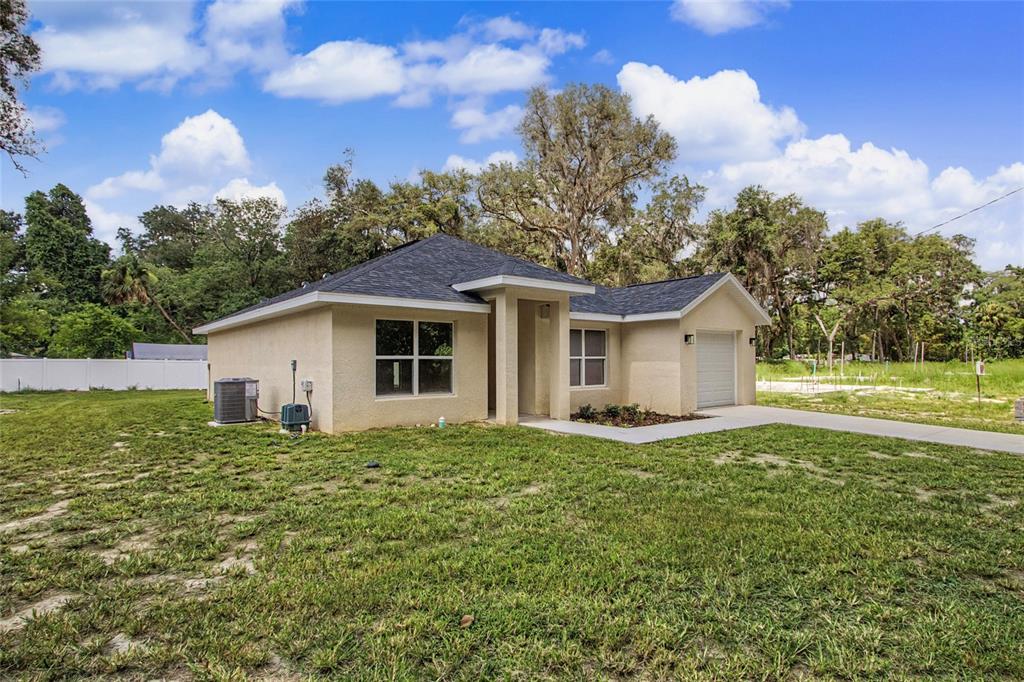 A single-story tan stucco house with a dark shingled roof and a one-car garage — 151 SE 81ST STREET, OCALA, FL