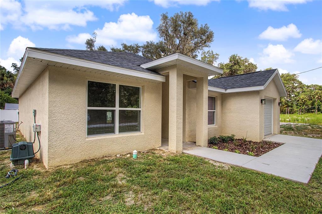 A single-story house with beige stucco siding, a dark shingled roof, and a concrete walkway — 151 SE 81ST STREET, OCALA, FL