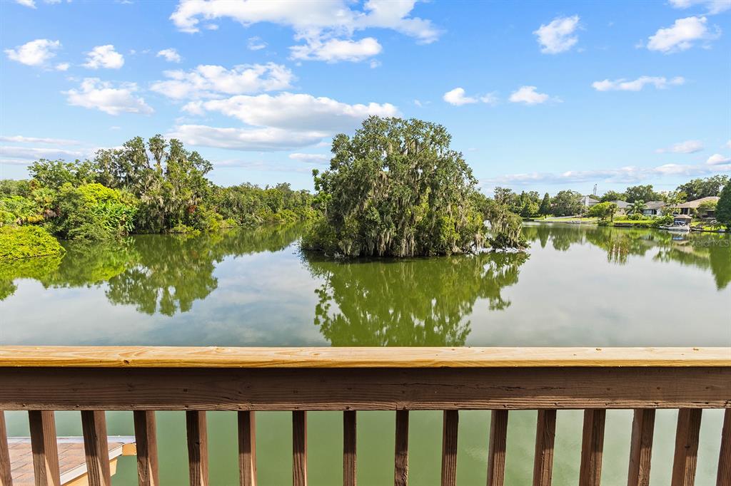 A wooden deck railing overlooks a calm lake with a small, tree-covered island — 614 MOUNTAIN LAKE PLACE, LAKELAND, FL