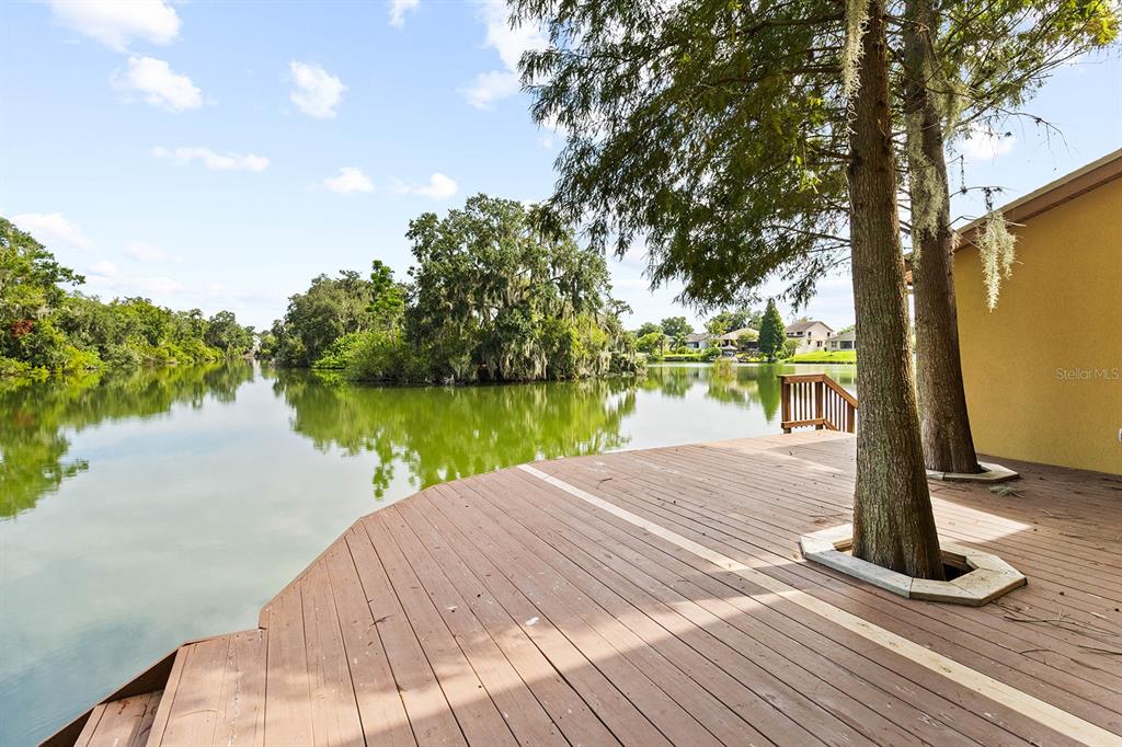 A wooden deck overlooks a calm lake with trees and houses in the background — 614 MOUNTAIN LAKE PLACE, LAKELAND, FL