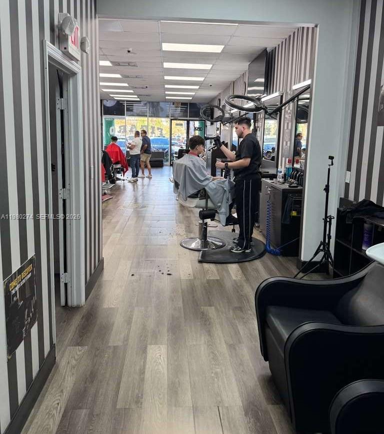 A barbershop interior features striped wallpaper, wood-look flooring, and multiple styling stations with chairs — Listing – Barbería Kendall, Kendall FL 33186, KENDALL, FL